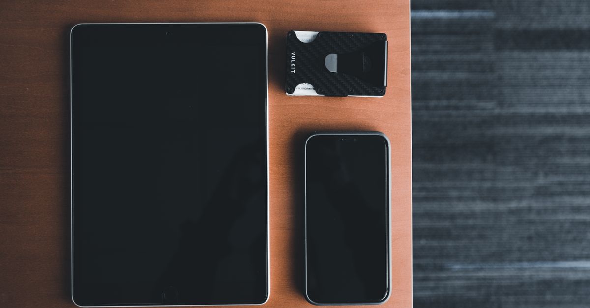 Top view of a tablet, smartphone, and card holder on a wooden surface, showcasing minimalist design.
